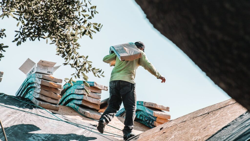 Werknemer draagt isolatiemateriaal tijdens dakrenovatie op een schuin dak met stapels bouwmateriaal.