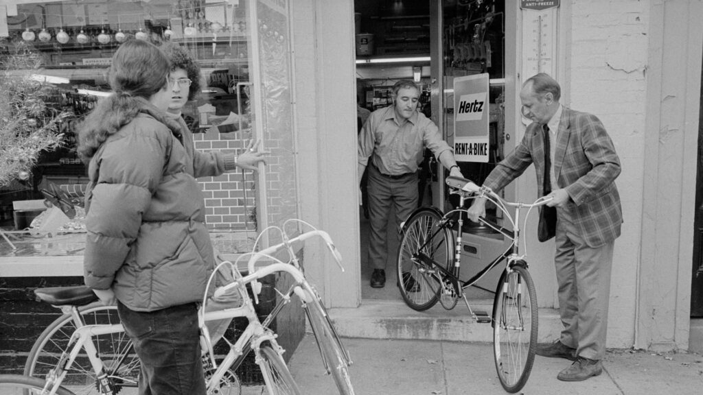 Verhuurders overhandigen een gehuurde fiets aan klanten bij een fietsverhuurwinkel