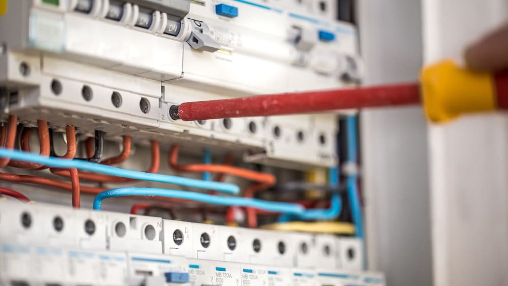 Elektricien gebruikt ge&iuml;soleerde schroevendraaier om zekeringen veilig te vervangen in een meterkast.