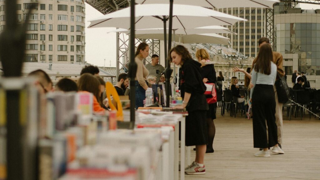 Bezoekers lopen langs stands met boeken en materialen tijdens een openlucht beursdeelname voorbereiden.