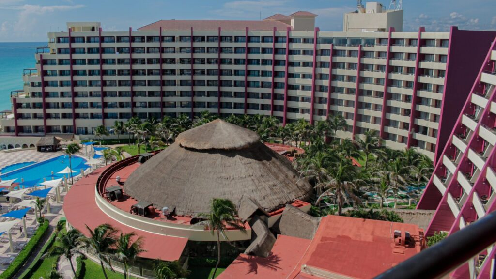 Luchtfoto van een hoteluitbreiding met extra kamers, zwembad en palmbomen bij de kust.
