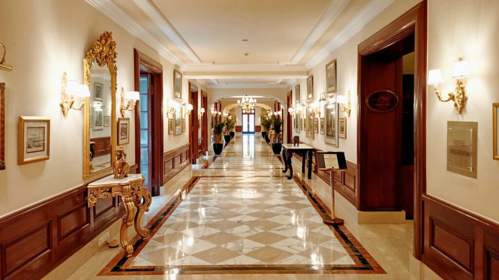 Luxe hotelgang met marmeren vloer, kroonluchters en decoratieve meubels na hoteluitbreiding.
