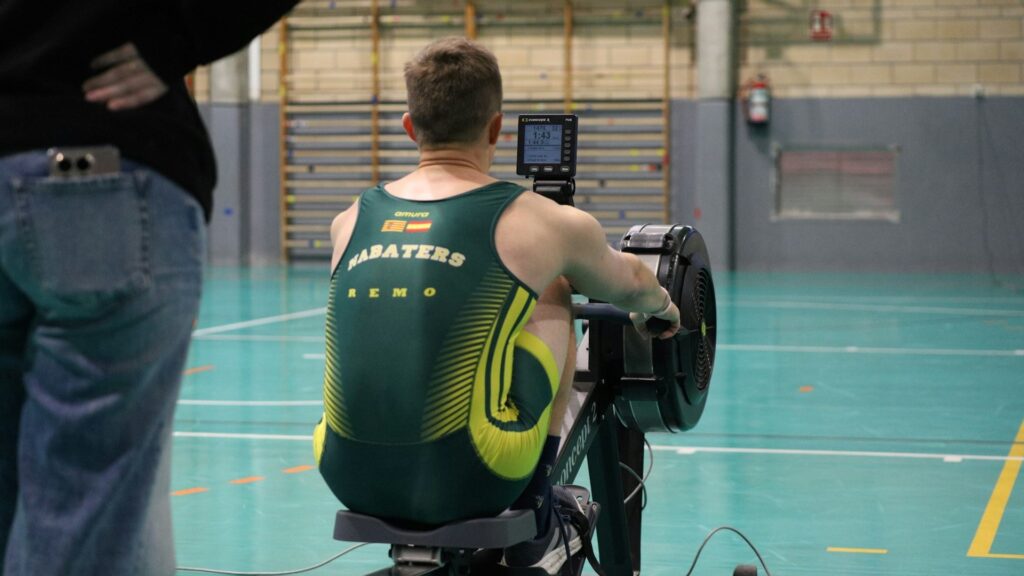 Sporter op roeimachine in sporthal tijdens training, passend bij trainingsbelasting verlagen en herstelmomenten