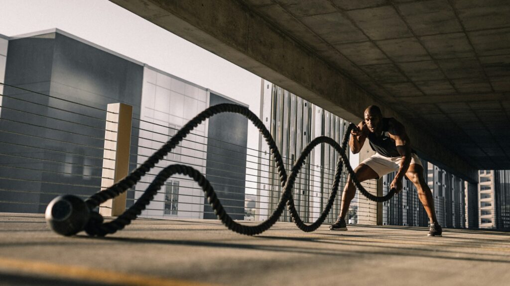 Man traint met battle ropes buiten, illustratie van zware inspanning en het belang van trainingsbelasting verlagen