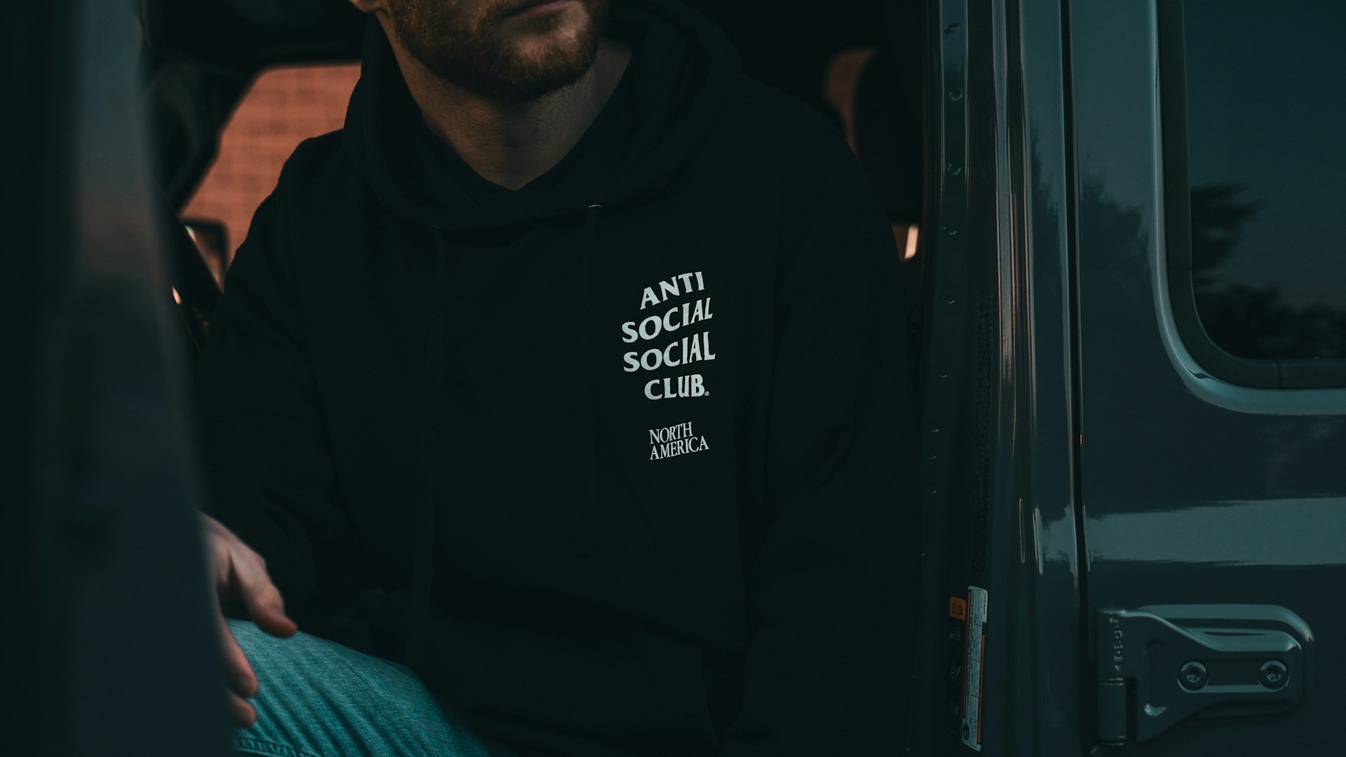 Zwarte hoodie met merkopdruk gedragen door persoon in voertuig met focus op print en stofkwaliteit
